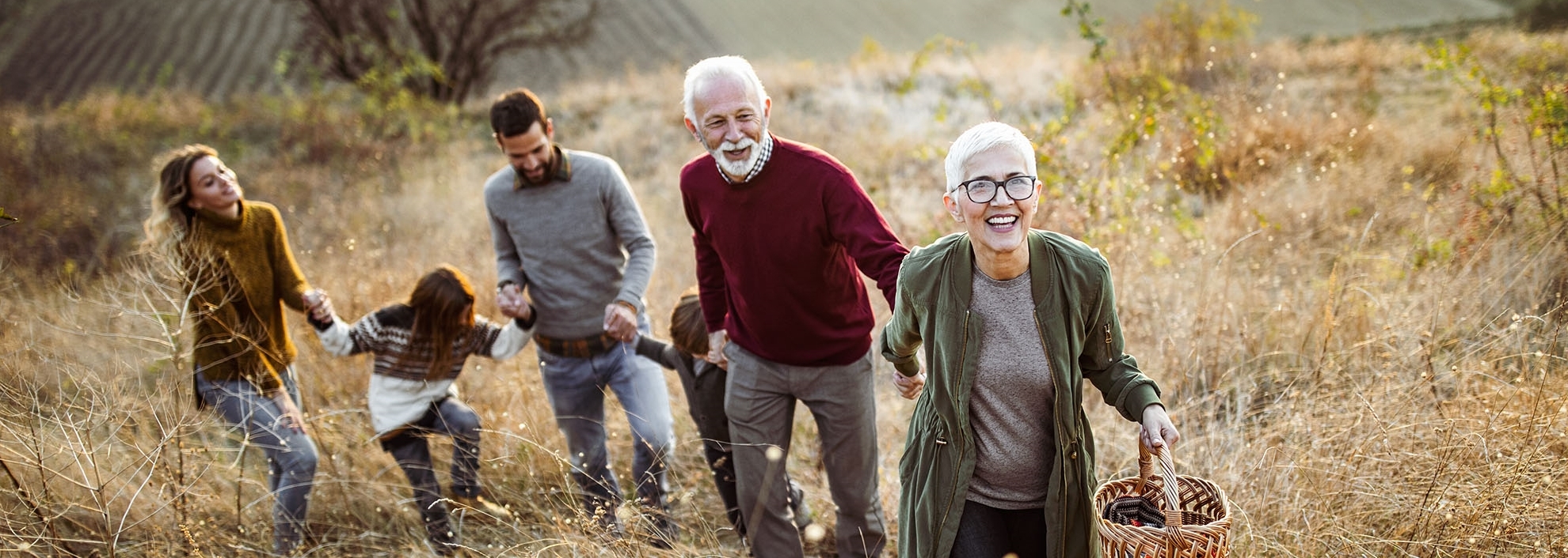 Happy generational family of Grandparents and father, son, daughter and wife holding hands in a field